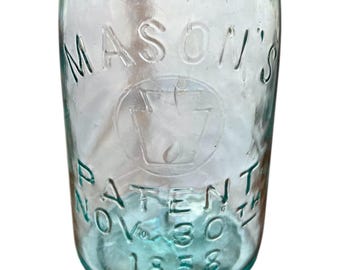 May include: A vintage, clear glass Mason's jar with embossed text. The jar features the words "MASON'S PATENT NOV 30TH 1858" and a central emblem. The glass has a slight blue-green tint.