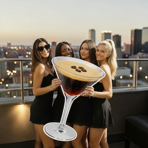Puede incluir: Cuatro personas sosteniendo un gran recorte de un espresso martini. La bebida tiene una parte superior cremosa con tres granos de café. Las personas visten vestidos negros en una azotea con un horizonte de la ciudad al fondo.