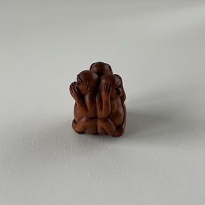 May include: A wooden sculpture depicting the three wise monkeys: See no evil, hear no evil, speak no evil. The monkeys are carved in a seated position, with their hands covering their eyes, ears, and mouth. The sculpture is a warm brown color.