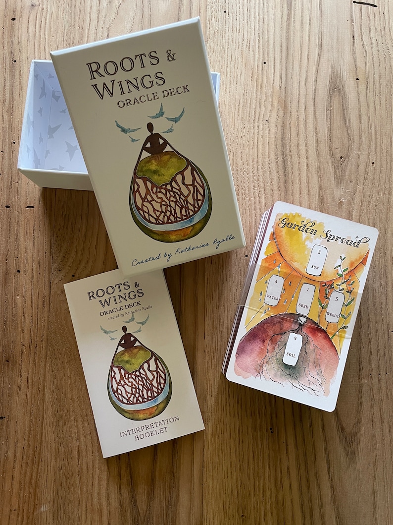 May include: A Roots & Wings Oracle Deck with a guidebook and a card spread layout. The deck features watercolor illustrations of a person sitting inside a tree with roots and wings. The card spread layout shows a garden with a sun, water, seed, soil, and weeds.