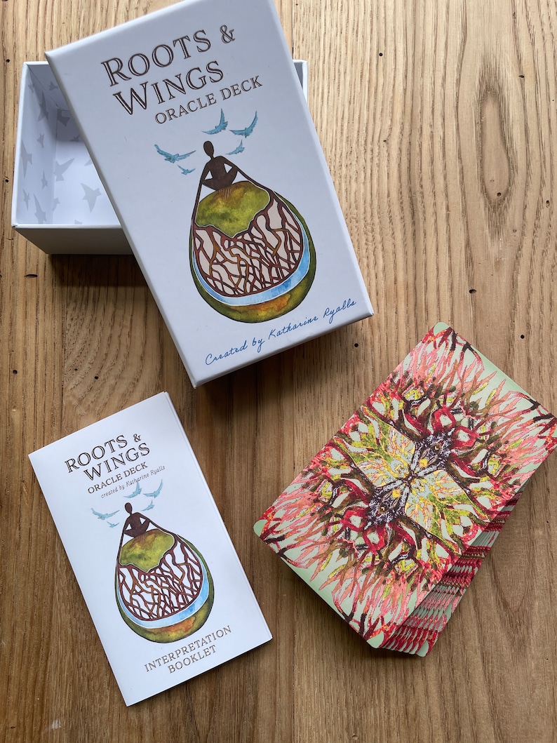 May include: A white box with the text "Roots & Wings Oracle Deck" and a colorful illustration of a person sitting on a tree root with birds flying above. The box is open and the deck of cards is visible. The cards have a colorful, abstract design.