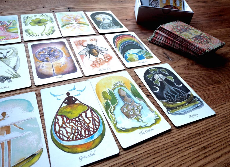 May include: A set of tarot cards with colorful illustrations and text. The cards feature images of nature, animals, and people. The cards are laid out on a wooden table.