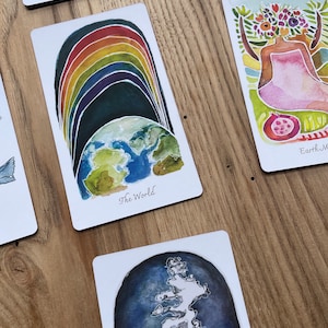 May include: A watercolor illustration of the world with a rainbow arching over it. The card is titled "The World".