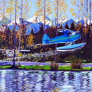 May include: A blue seaplane flies over a lake with a backdrop of snow-capped mountains and autumn foliage.