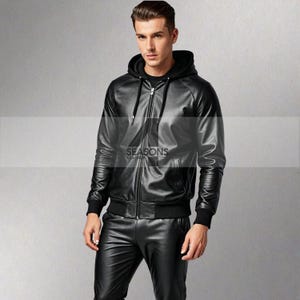 Puede incluir: Chaqueta con capucha de cuero negro con cremallera, pu&ntilde;os y dobladillo acanalados. El logo "SEASONS LEATHER" es visible. El modelo lleva pantalones de cuero negro. Una opci&oacute;n de abrigo elegante.