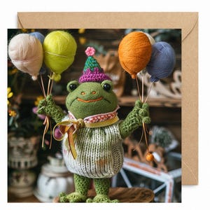 May include: A handmade greeting card featuring a knitted frog holding yarn balloons. The frog is wearing a party hat and a sweater. The balloons are in shades of pink, yellow, orange, and blue. The card is on a brown envelope.