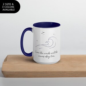 May include: White ceramic mug with a navy blue interior and handle. The mug features a line drawing of a wave and the text "Even the winds and the waves obey Him."