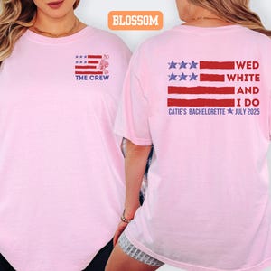 May include: A light pink t-shirt with a graphic design on the front and back. The front features a red, white, and blue design with the text "THE CREW". The back has a similar design with the text "WED WHITE AND I DO CATIE'S BACHELORETTE JULY 2025".