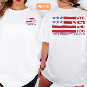 May include: White t-shirt with a patriotic design. The front features a small American flag with the text "THE BRIDE." The back displays a larger flag design with the words "WED WHITE AND I DO" and "CATIE'S BACHELORETTE JULY 2025."