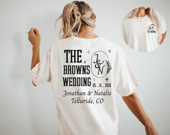 May include: Cream-colored t-shirt with a black graphic design for "The Browns Wedding." The design includes the couple's initials, wedding date, and location. The shirt is a casual style.