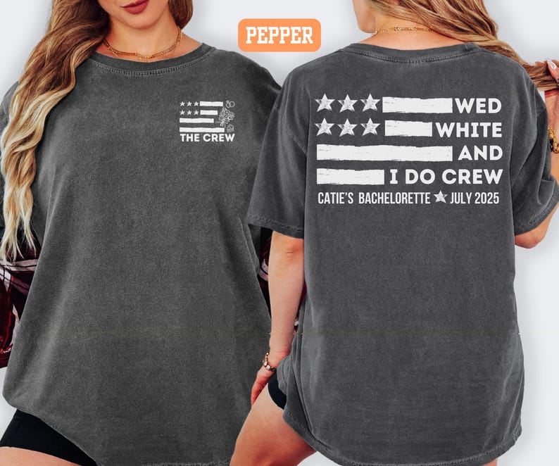 May include: Dark gray t-shirt with a white and gray flag design and the text "THE CREW" on the front. The back of the shirt features the text "WED WHITE AND I DO CREW" and "CATIE'S BACHELORETTE JULY 2025".