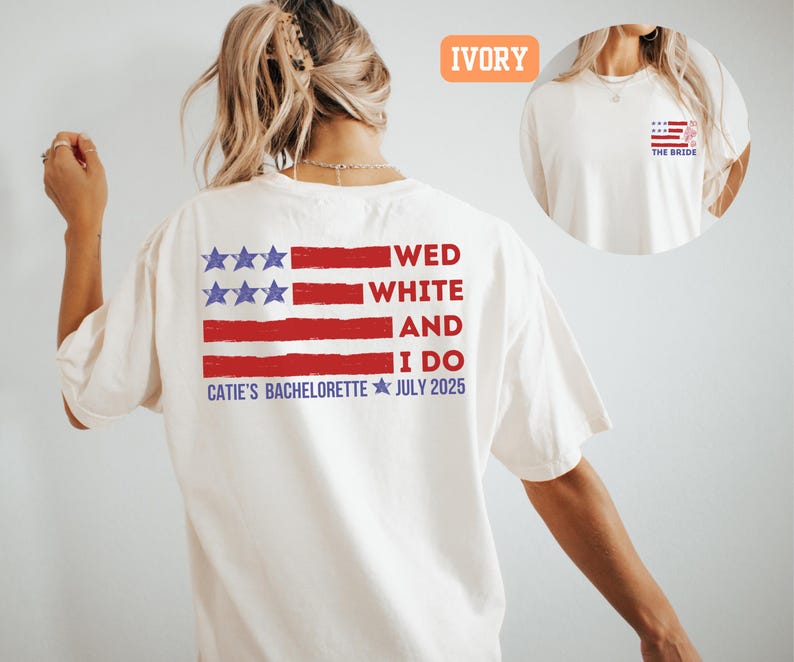 May include: Ivory-colored t-shirt with a patriotic design. The back features a red, white, and blue American flag graphic with the text "WED WHITE AND I DO" and "CATIE'S BACHELORETTE JULY 2025". A smaller flag design is on the front.