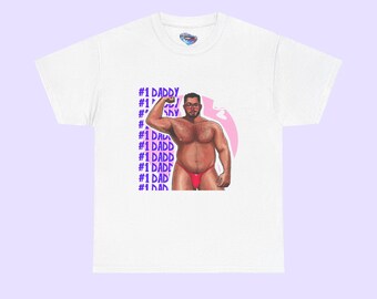 May include: White t-shirt featuring a graphic of a muscular man in red underwear, flexing his arm. The text "#1 DADDY" is repeated in a vertical pattern on the left side of the shirt. The design includes a pink oval and a blue logo.