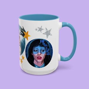 May include: White ceramic mug with a blue interior and handle. The mug features a portrait of a woman with blue face paint and the text "YOU SAID FORGIVE AND FORGET SO GET ME OUT OF THIS MESS". Gold and silver star accents.