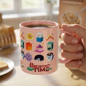 May include: A pink ceramic mug filled with coffee, decorated with cartoon breakfast food and character graphics. The mug has a pink handle and the words "BREAKFAST TIME" printed on it. Steam rises from the coffee.