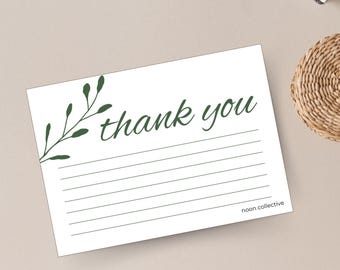 May include: A white thank you card with a green leafy branch design and the text "thank you" in cursive. The card has lined space for writing and the text "noon collective" at the bottom.