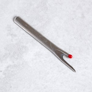 May include: A silver crochet hook with a red tip. The hook is designed for use with yarn or thread.
