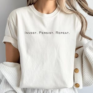 Könnte beinhalten: Weißes T-Shirt mit dem Aufdruck "INVEST. PERSIST. REPEAT." in Schwarz.