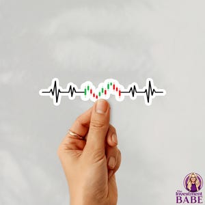 May include: A white sticker featuring a black heartbeat line with a stock market graph in the center, showing green and red candlesticks. The sticker is held by a hand with a gold ring.