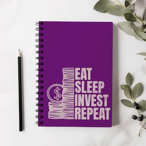 Può includere: Blocco notes a spirale viola con una grafica bianca di una pila di monete con un segno di dollaro in cima e il testo "Eat Sleep Invest Repeat".