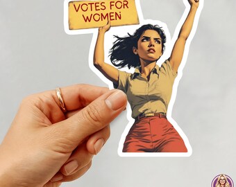 May include: A sticker featuring a woman holding a sign that reads "VOTES FOR WOMEN." She is wearing a tan shirt and red pants, with her fist raised in the air. The sticker is held by a hand.