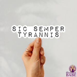 May include: A white sticker with the text "SIC SEMPER TYRANNIS" in black, held by a hand with a gold ring. The sticker has a black border and is against a light gray background. The Investment Babe logo is in the bottom right corner.