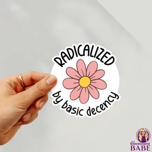 Puede incluir: Una pegatina blanca con el texto "RADICALIZED" sobre una margarita rosa con centro amarillo, y las palabras "by basic decency" debajo. El logotipo de The Investment Babe está en la esquina inferior derecha.