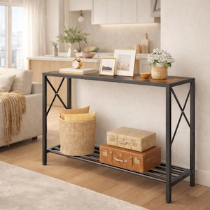 May include: A black metal and wood console table with a lower shelf. The table has a rectangular top with a brown wood finish. Decorative items include framed photos, a small clock, and a vase of flowers. A woven basket and suitcases are on the lower shelf.