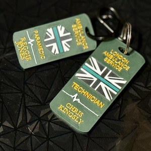 May include: Two green keychains featuring the Union Jack flag and text for the London Ambulance Service. One reads "Paramedic" and "Reggie Jones." The other says "Technician" and "Chris Kingsley."