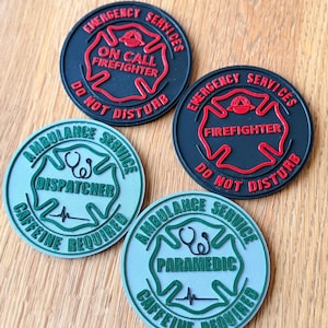 May include: Four round patches with emergency service themes. Two black patches read "Emergency Services, Firefighter, Do Not Disturb." The other two are light blue and read "Ambulance Service, Dispatcher, Caffeine Required" and "Paramedic, Caffeine Required."