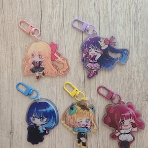 May include: Five acrylic keychains featuring chibi-style anime characters with colorful hair and outfits. Each charm includes a matching plastic lobster clasp in pink, purple, blue, yellow, or magenta, showcasing distinct character designs and expressions.