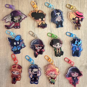 May include: A collection of acrylic keychains featuring various cartoon characters. Each keychain has a unique design with vibrant colors and attached metal hardware. The characters include figures with hats, capes, and other accessories.
