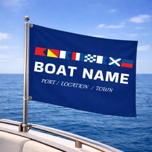 May include: A dark blue rectangular flag attached to a silver metal pole. The flag features a row of colorful nautical signal flags at the top, the white text BOAT NAME in a bold font, and the white text PORT / LOCATION / TOWN in a smaller font.