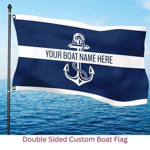 May include: A navy blue boat flag with a white stripe and anchor design. The flag reads "YOUR BOAT NAME HERE" in white text. The flag is double-sided and is displayed on a pole over the ocean.