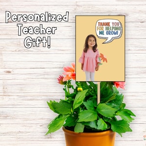 Op de afbeelding: Een gepersonaliseerd cadeau voor een leraar met een plant en een bord met de tekst "Bedankt voor het helpen met groeien!" met een foto van een jong meisje dat een bloem vasthoudt.