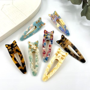 Può includere: Set di sette fermagli per capelli a forma di gatto colorati. I fermagli sono in plastica e hanno un effetto marmorizzato. Ogni fermaglio ha un design a forma di gatto dorato.