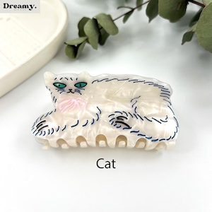 May include: White cat hair clip with blue and black outline. The cat is laying down with a pink bow. The clip is labeled "Cat".