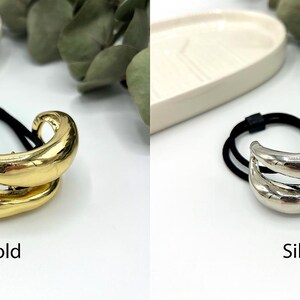 Pu&ograve; includere: Due elastici per capelli con un design astratto in oro e argento. Gli elastici sono realizzati con un elastico nero con un accento metallico.