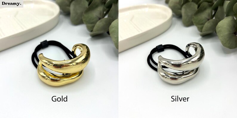 Pu&ograve; includere: Due elastici per capelli con un design astratto in oro e argento. Gli elastici sono realizzati con un elastico nero con un accento metallico.