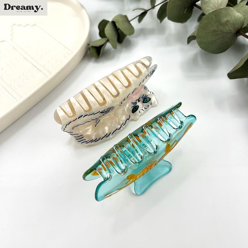 May include: Two hair clips, one white with a cat design and one blue with a floral design.