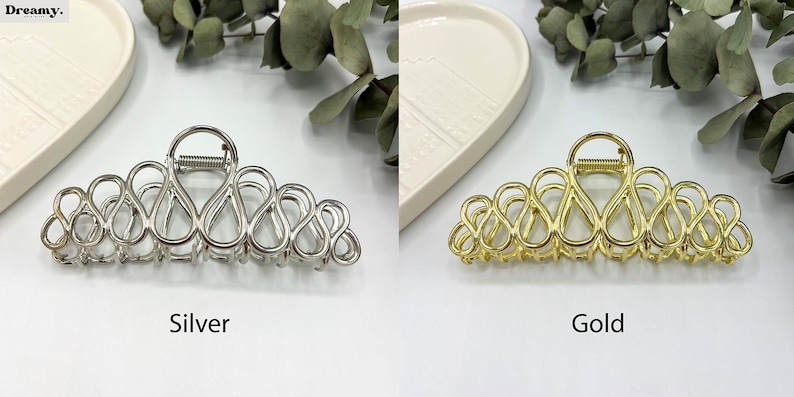 May include: Silver and gold-coloured hair claw clips. The clips have an open, looped design. The silver clip is on the left, and the gold clip is on the right. The word "Silver" is below the silver clip, and the word "Gold" is below the gold clip.