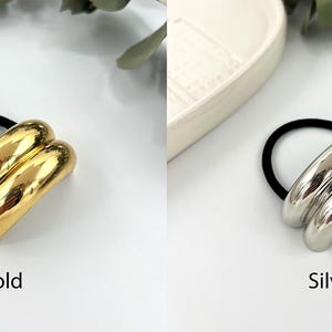 May include: Two hair ties with a double-layered, smooth, rounded metal design. One is gold and the other is silver.