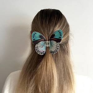 May include: A butterfly hair clip with teal and black wings, held in place with a clear clasp, is in the hair. The clip features detailed wing patterns. The word "Dreamy" is in the top left corner.