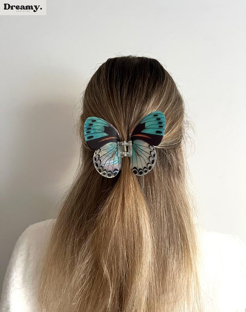 May include: A butterfly hair clip with teal and black wings, held in place with a clear clasp, is in the hair. The clip features detailed wing patterns. The word "Dreamy" is in the top left corner.