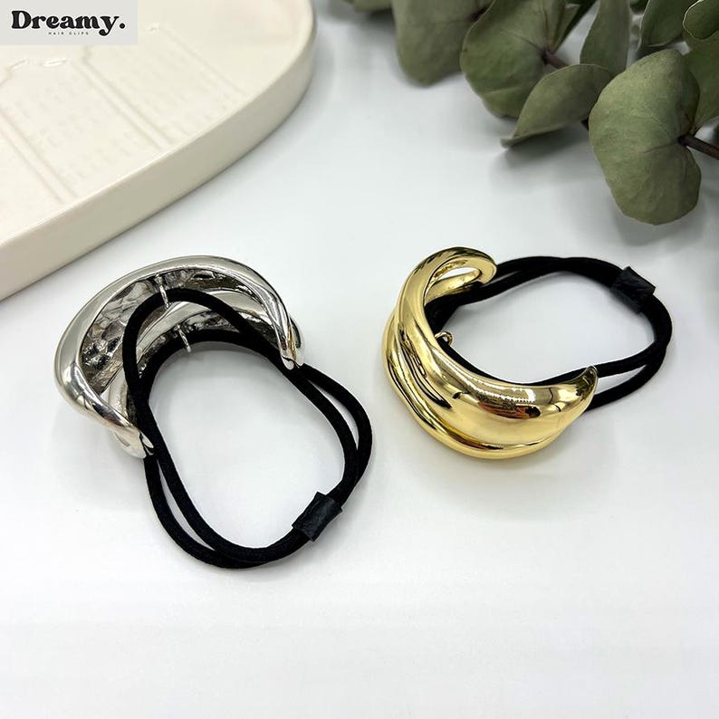 Pu&ograve; includere: Due elastici per capelli con un design in metallo dorato e argentato. Gli elastici hanno bande elastiche nere.