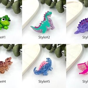 K&ouml;nnte beinhalten: Sechs verschiedene Stile von bunten, glitzernden, plastischen Dinosaurier- und Cham&auml;leon-Broschen. Die Broschen sind alle in verschiedenen Farben und haben eine glitzernde Oberfl&auml;che.