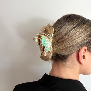 May include: A gold-colored butterfly hair clip with a turquoise and red design. The hair accessory is clipped into a bun. The word "Dreamy" is in the top left corner.
