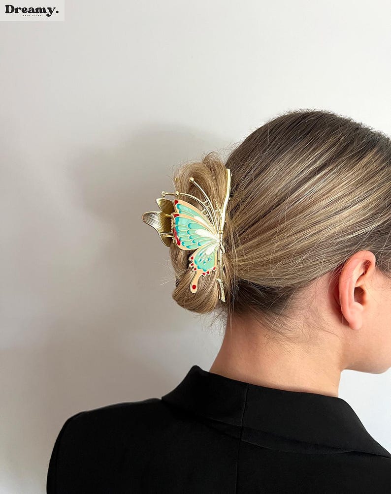 May include: A gold-colored butterfly hair clip with a turquoise and red design. The hair accessory is clipped into a bun. The word "Dreamy" is in the top left corner.