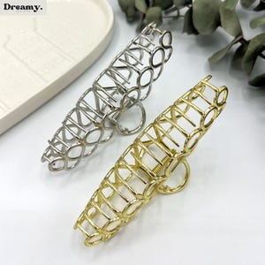 May include: Two metal hair claw clips, one silver and one gold, are shown. The clips feature an open, geometric design with a circular pattern. The word "Dreamy" is visible in the top left corner.