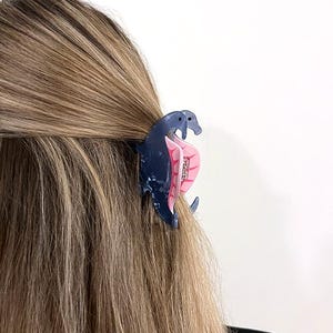 K&ouml;nnte beinhalten: Eine blaue und rosafarbene Plastik-Haarklammer in Form eines Seepferds. Die Klammer h&auml;lt das lange, hellbraune Haar einer Frau.